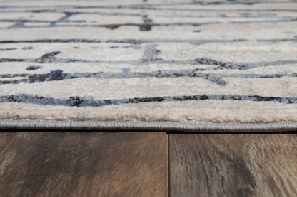 Close-up of light gray rug with blue abstract pattern and bound edge on dark wood floor.