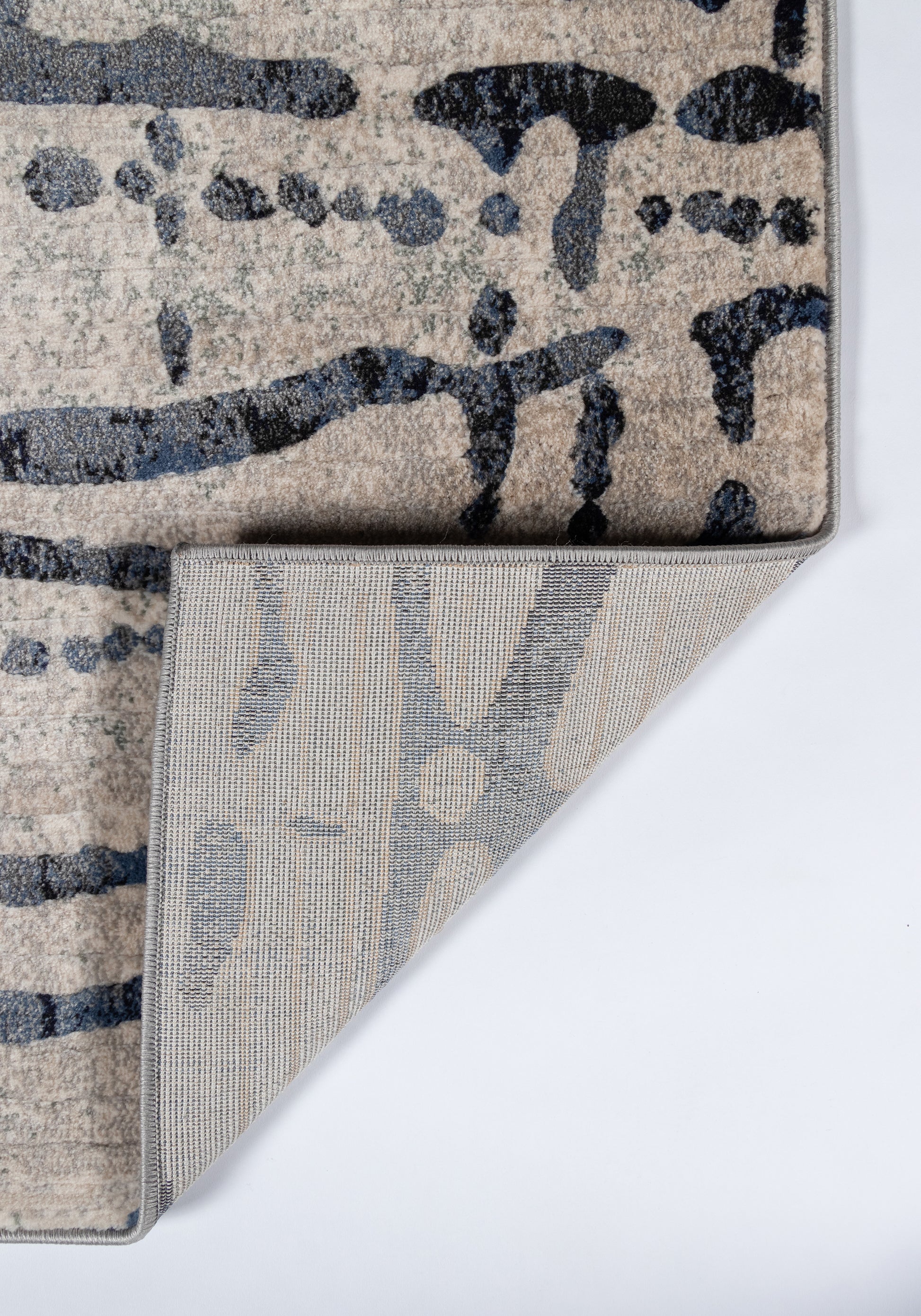 Abstract gray and beige runner rug with navy brushstroke pattern; plush pile, folded corner reveals gray underside.