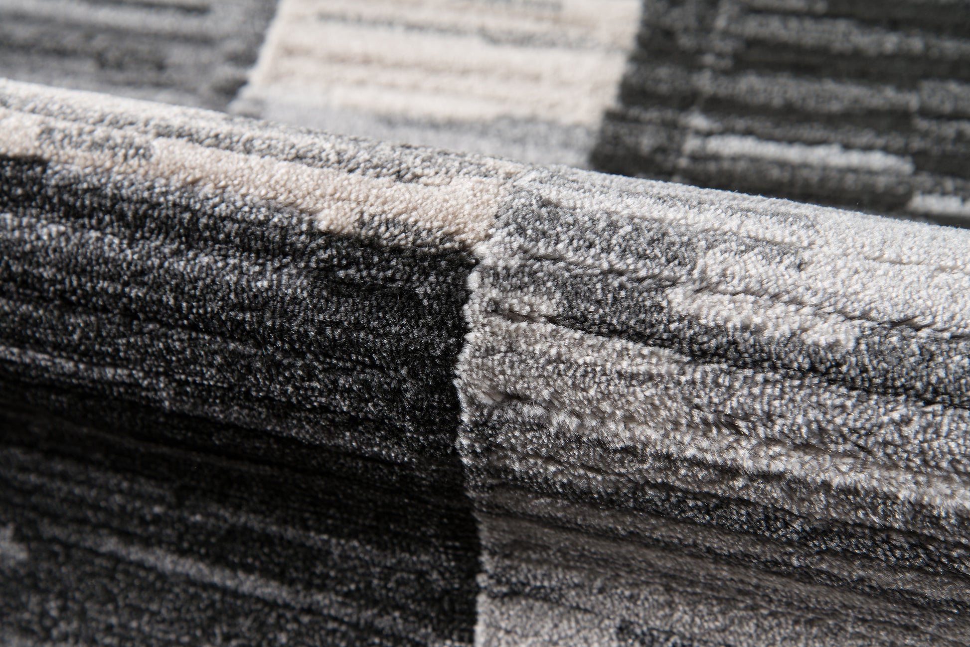 Close-up of a textured charcoal-gray and light-gray rug with thick pile and geometric block pattern; modern, cozy accent.