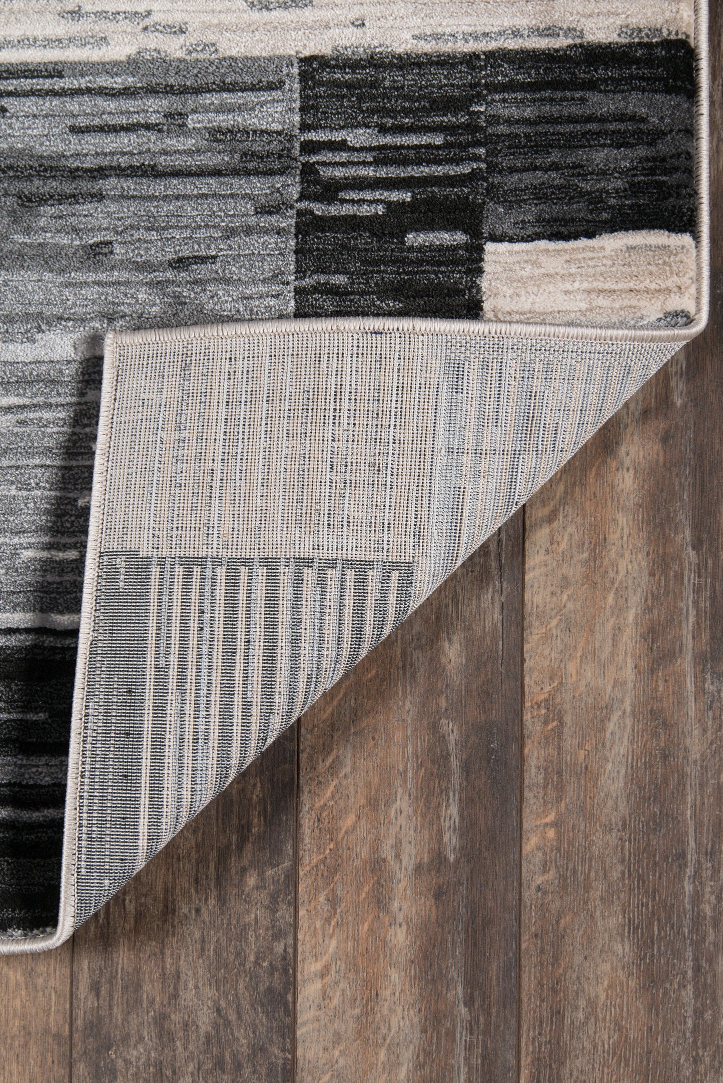 Patchwork modern area rug in black, gray & white; striped underside shown by folded corner on a wood floor.