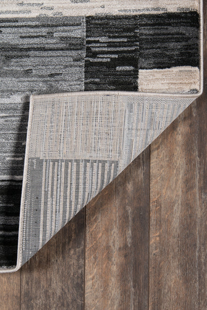 Patchwork modern area rug in black, gray & white; striped underside shown by folded corner on a wood floor.