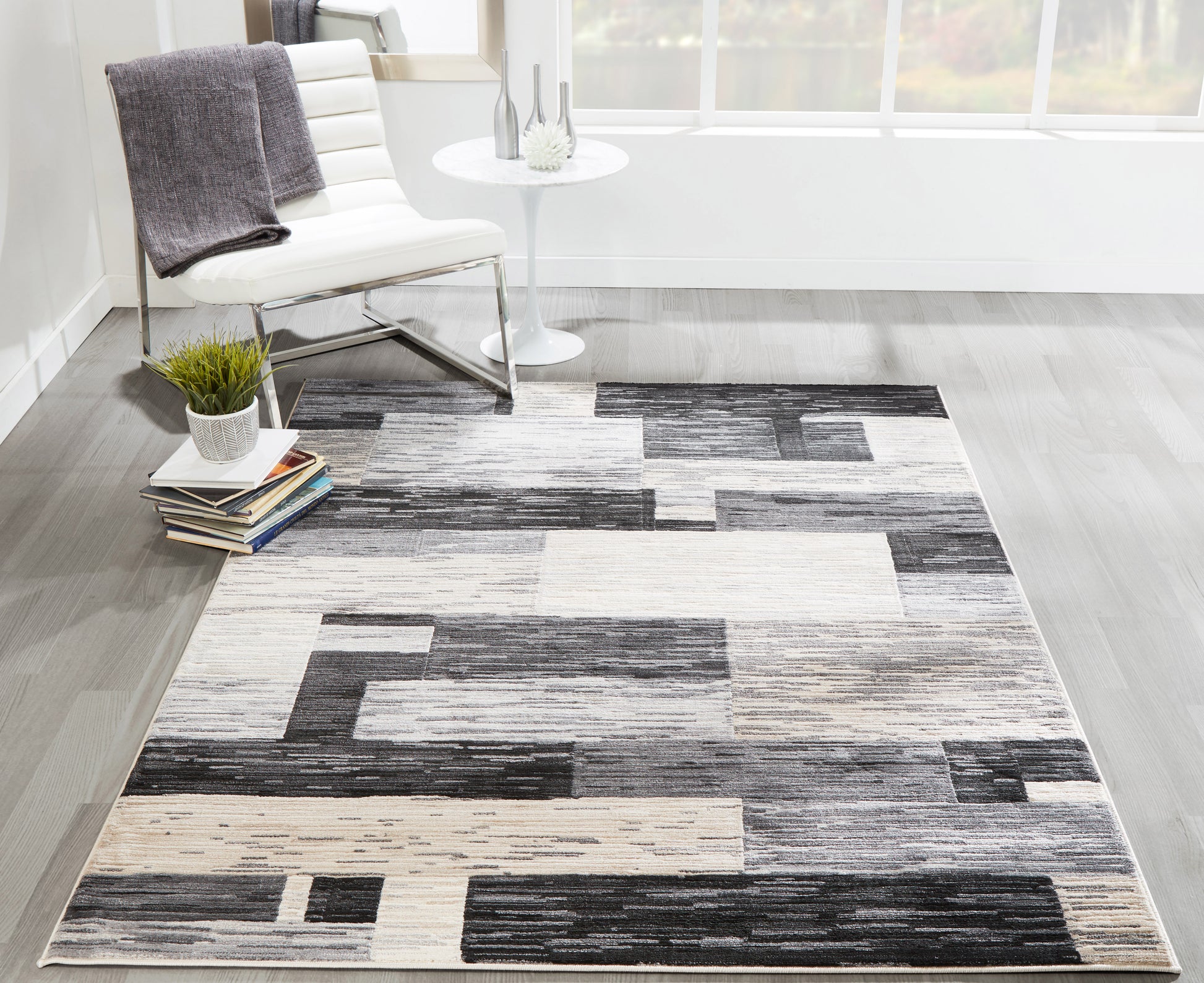 Geometric area rug in grayscale beige blocks; modern living room with white chair and round side table.