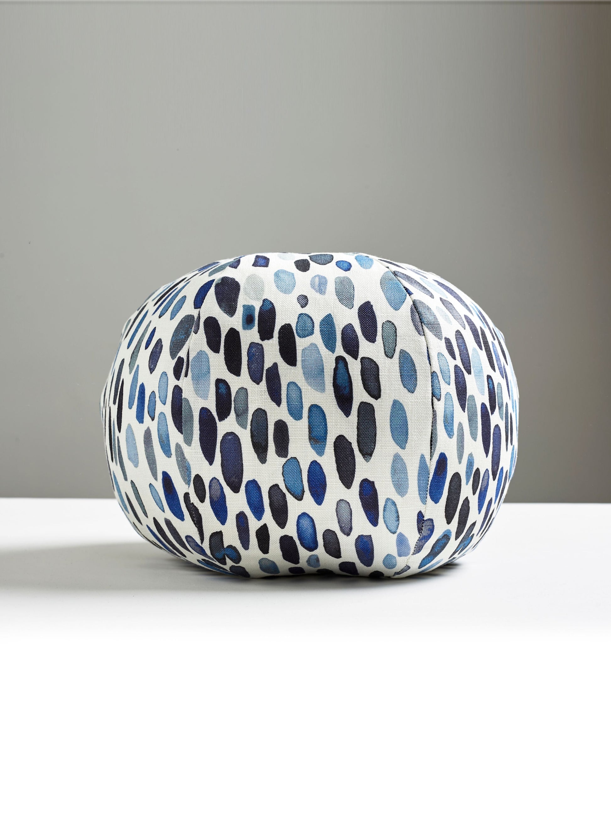 Round decorative pillow with an abstract blue dots and circles graphic on white fabric.