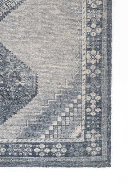Blue-gray woven rug with a large geometric medallion, stepped borders, and a dotted floral edge.