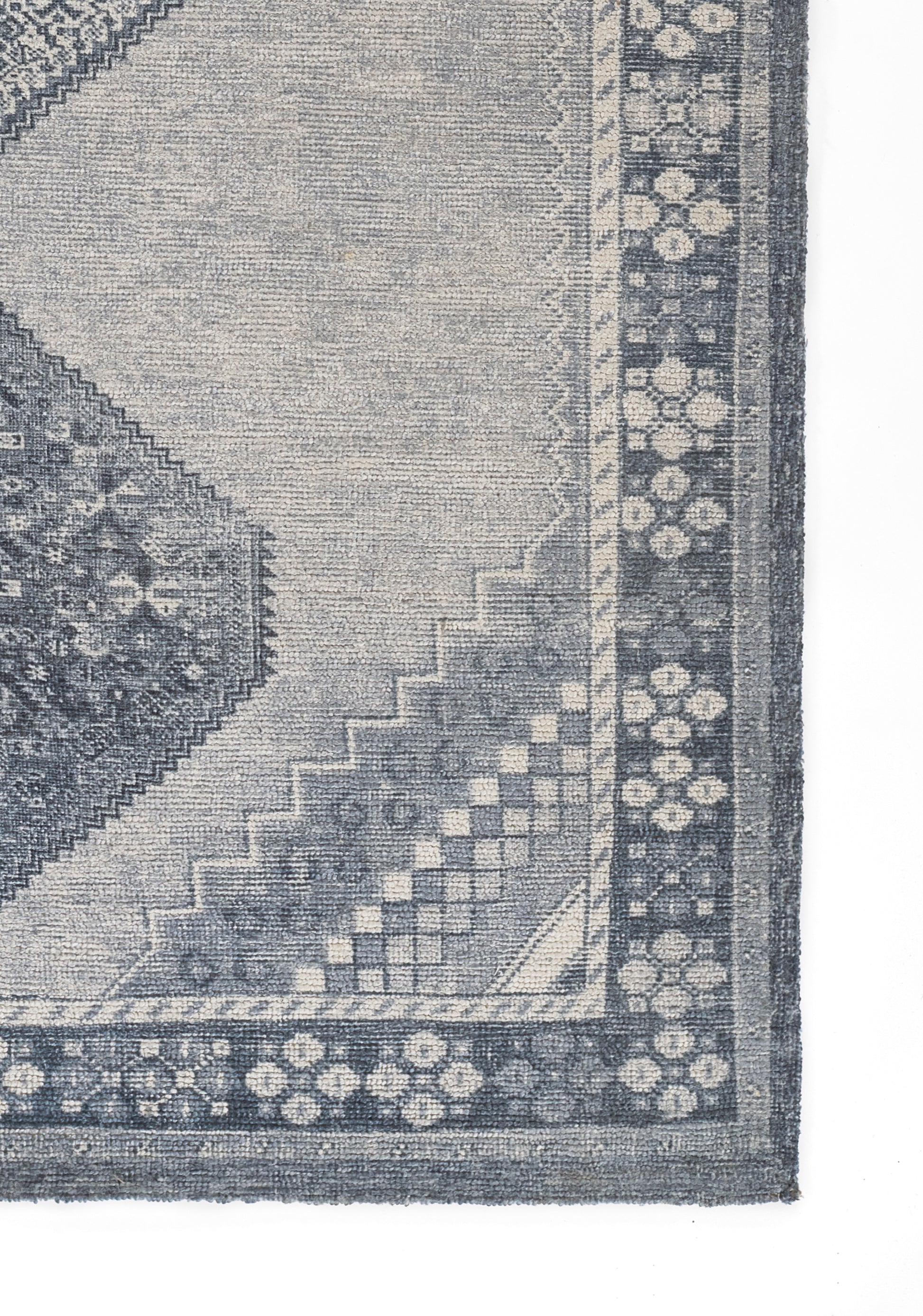 Blue-gray rug featuring a distressed geometric pattern with diamonds and a decorative floral border.