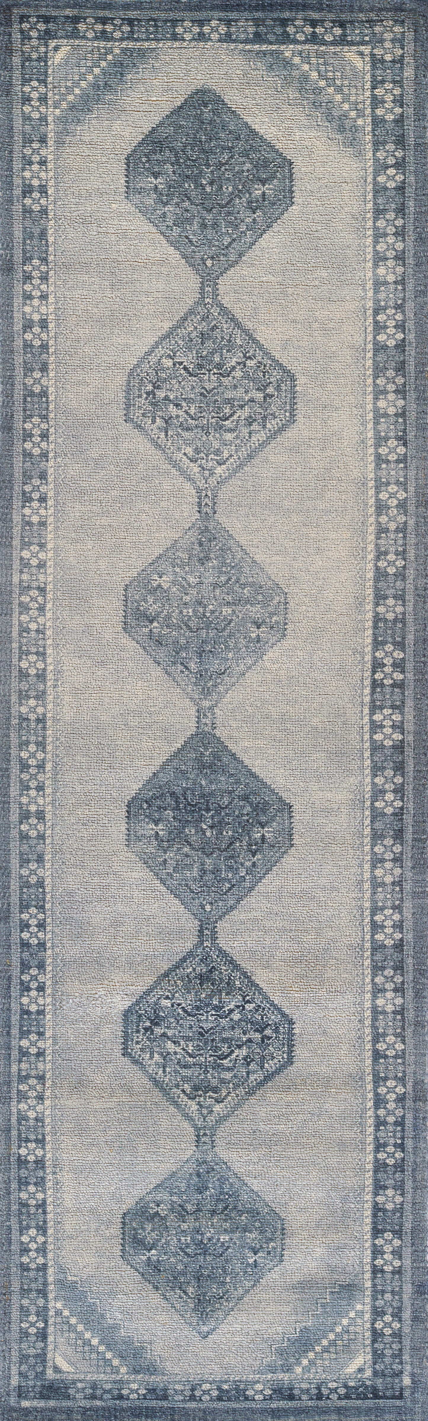 Blue-toned runner rug with stacked diamond motifs along a beige field and floral border.