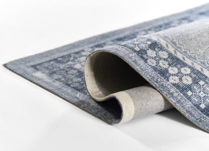 Blue-gray patterned area rug, partially rolled, soft woven texture with subtle floral motif for modern home decor.