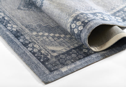 Blue-gray patterned rug with geometric/medallion print, partially rolled to reveal beige underside.