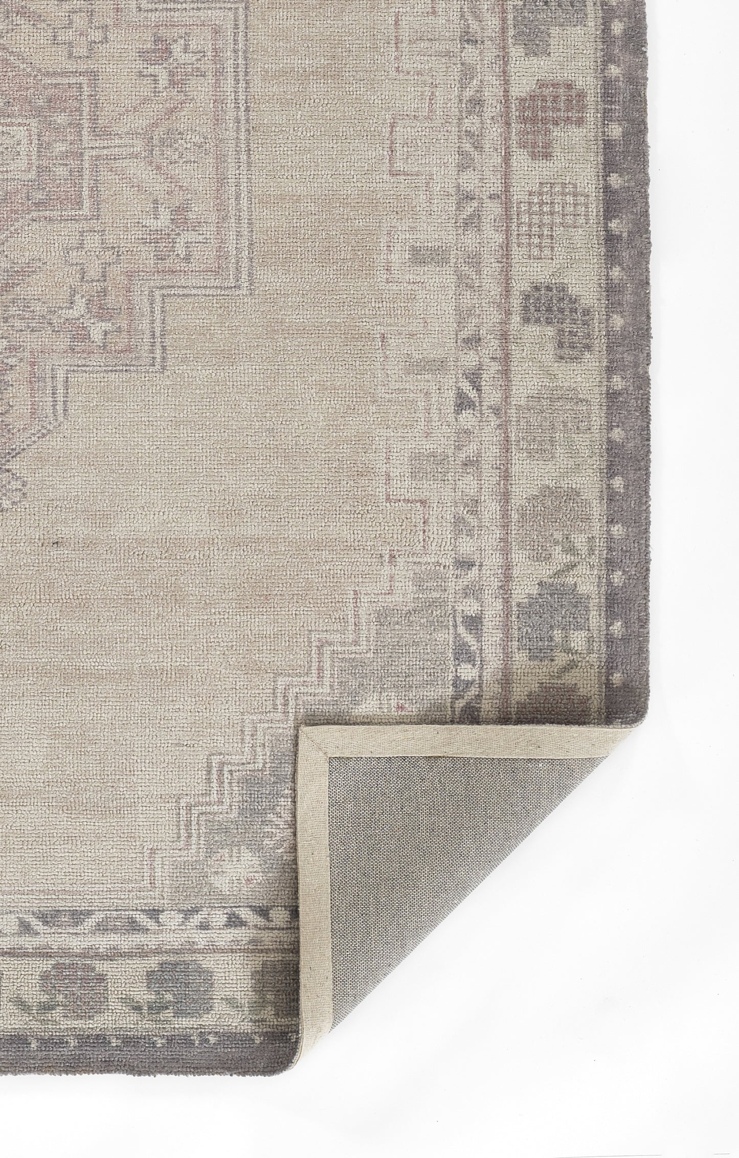 Beige oriental rug with muted pink-gray border, corner folded to reveal gray underside.