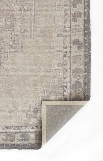 Beige oriental rug with muted pink-gray border, corner folded to reveal gray underside.