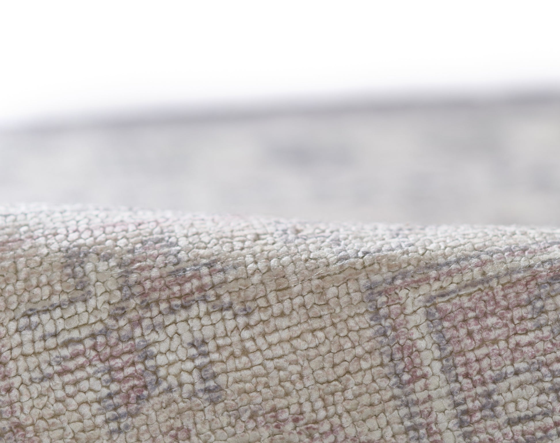 Close-up of a textured woven rug with cream and beige loop pile and subtle pink and blue geometric pattern.