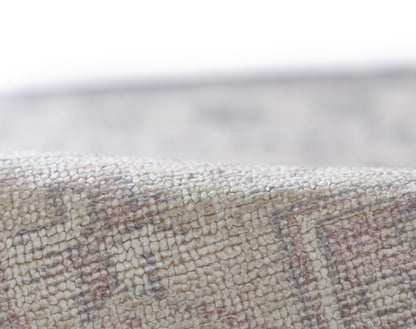Close-up of a cream woven rug with pink and gray geometric pattern and soft loop-pile texture.