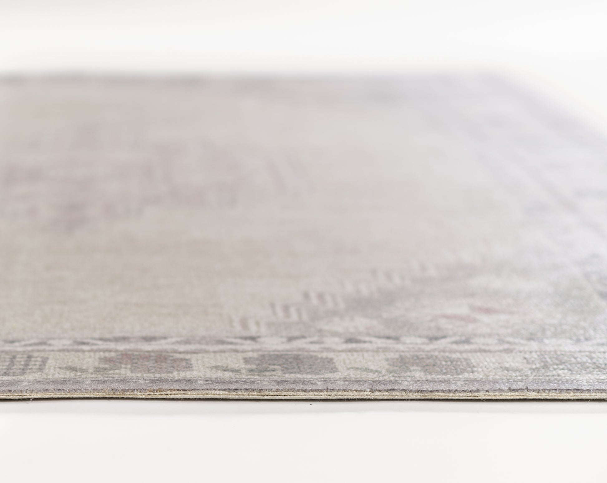 Beige and gray flat-weave rug with subtle geometric border, edge-on view.