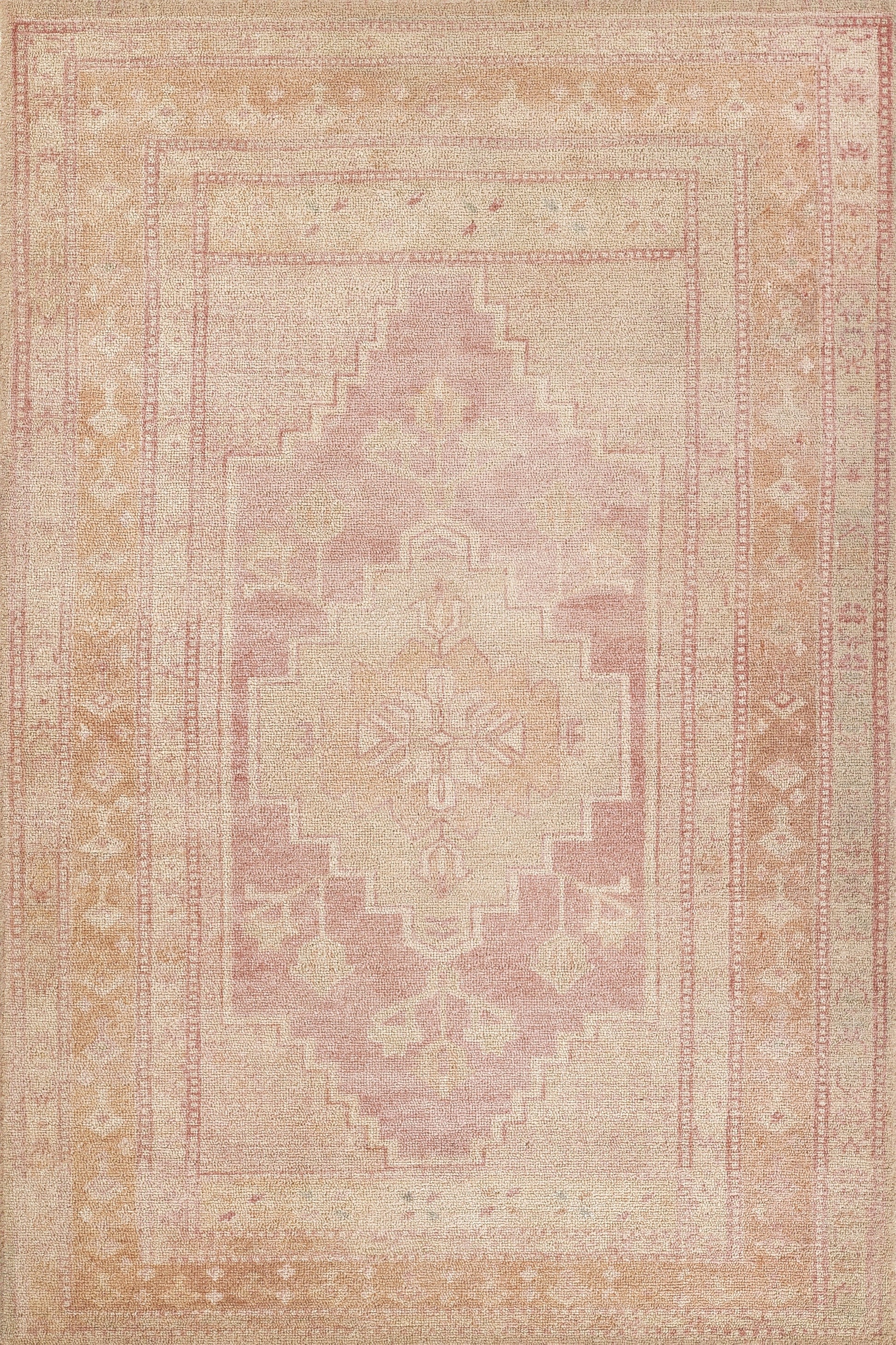 Pastel pink & peach distressed woven area rug with a geometric central medallion & ornate border.