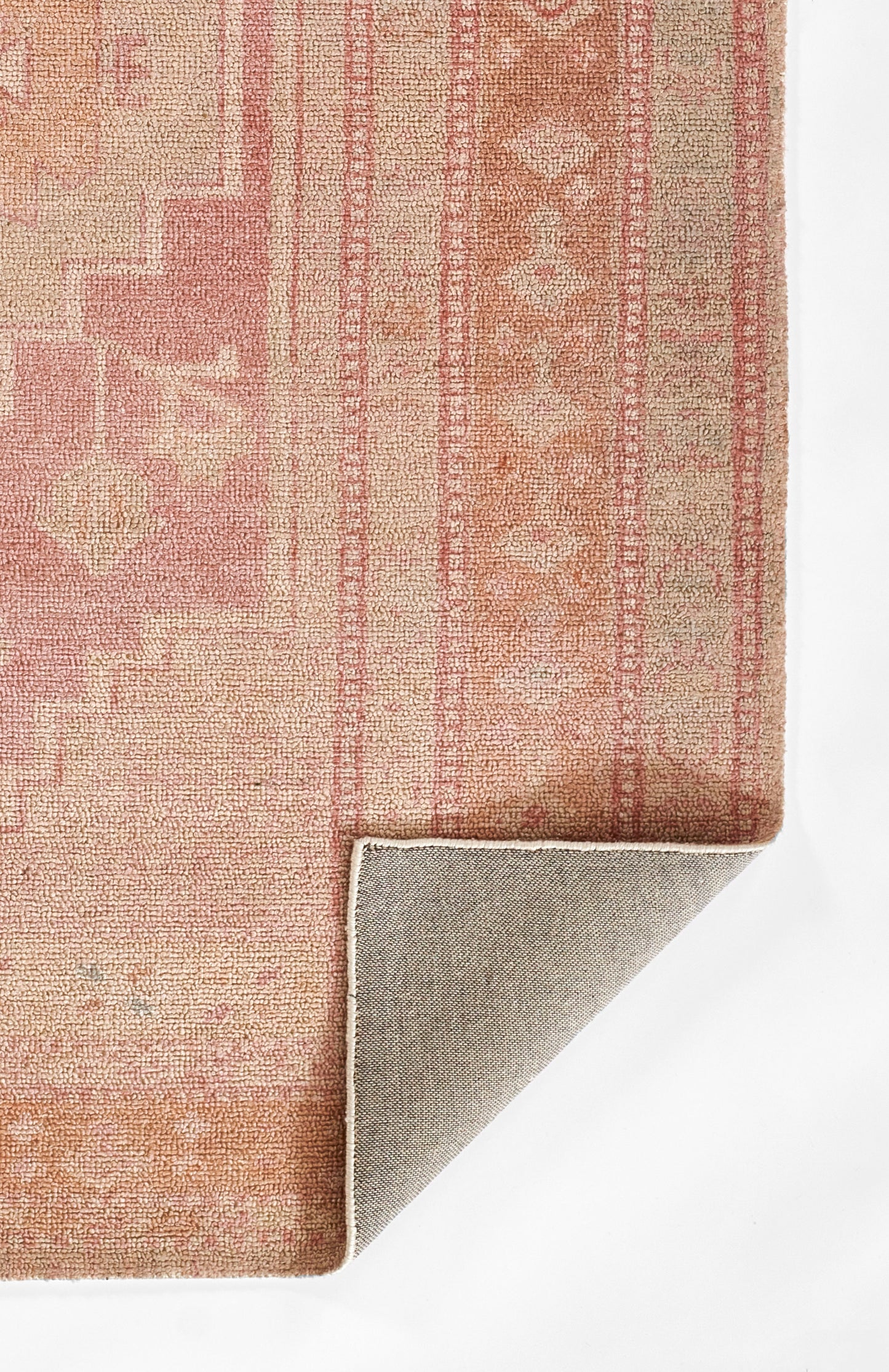 Coral-pink vintage-style woven rug with geometric border pattern; soft textured pile, folded corner shows gray backing.