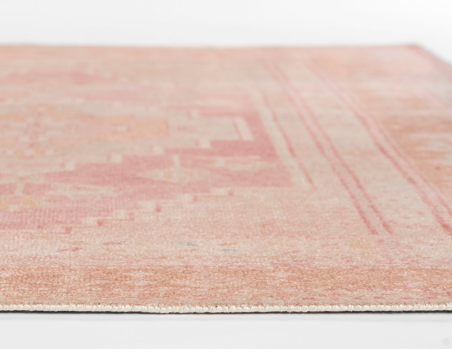 Pink vintage-style flat-weave rug with a geometric pattern and cream fringe along the edge.