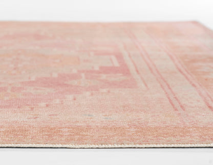 Soft pink-peach area rug with subtle vintage pattern and white fringe edge.