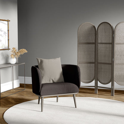 Modern charcoal armchair with beige cushion on a circular white rug in a gray living room, with a three-panel woven rattan screen and wooden floor.