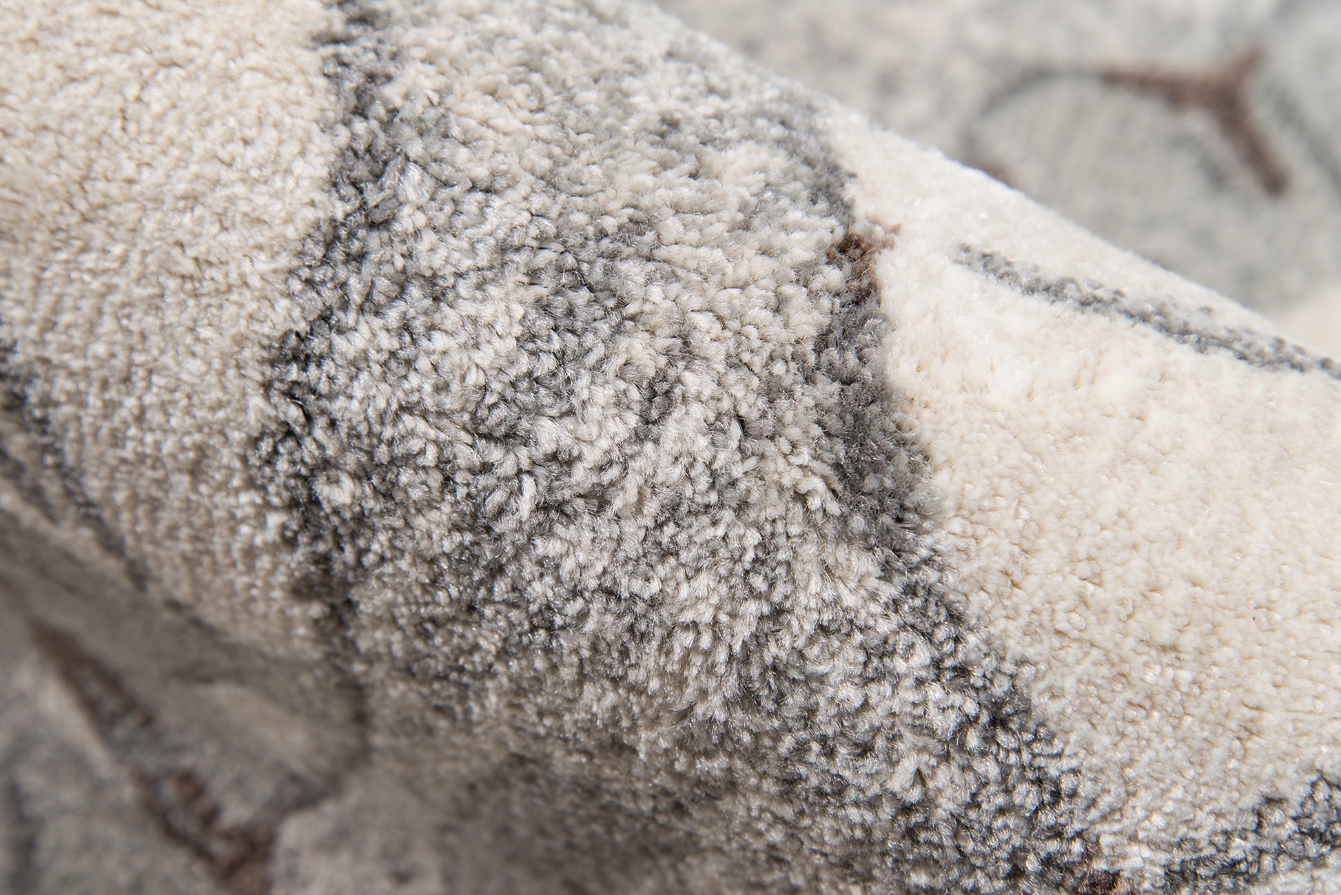 Close-up of a plush beige-gray rug with dense shag pile and subtle geometric lines.