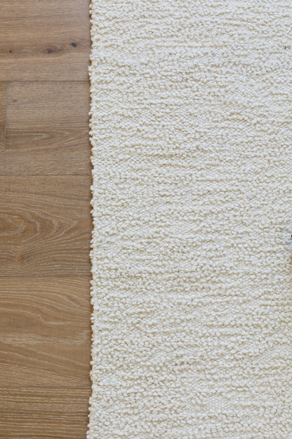 Cream shag/boucle rug with dense loop pile on warm brown wooden floor.