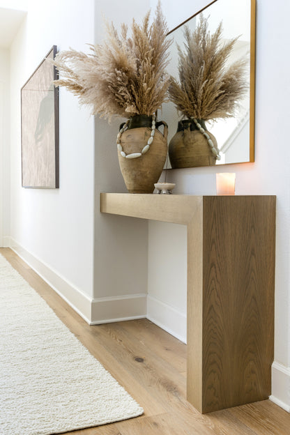 Wooden console table with two beige ceramic vases and pampas grass in a minimalist entryway.