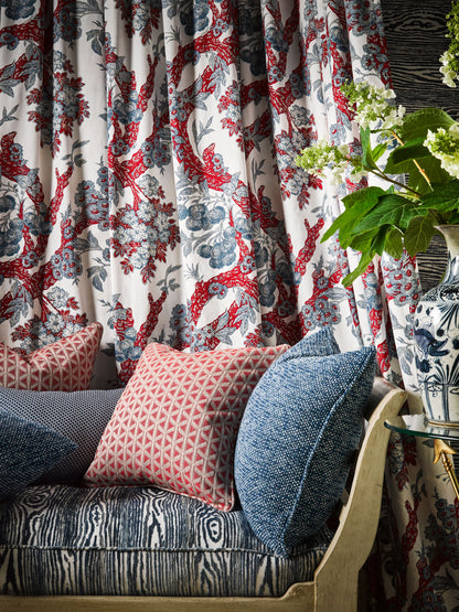 Floral red-blue curtains over a blue patterned sofa with pink diamond cushions and a blue-and-white vase with greenery.