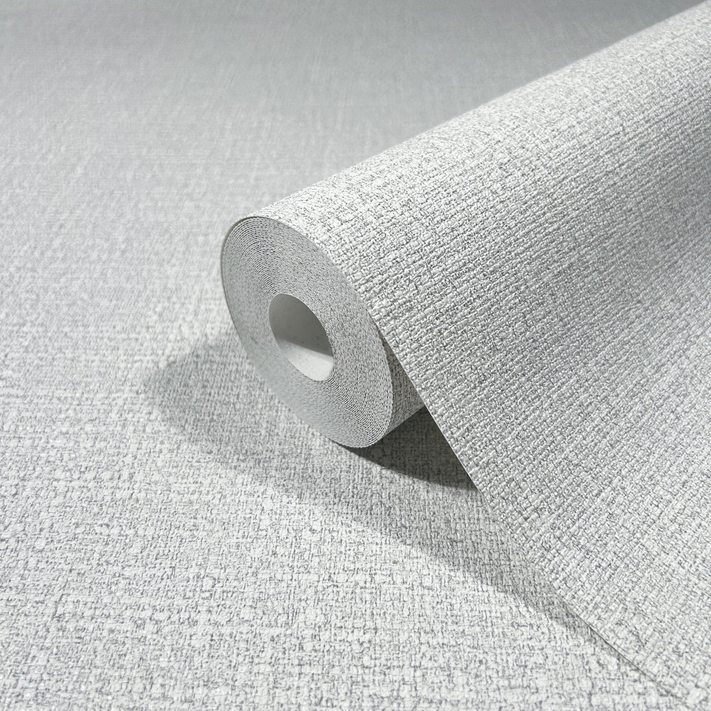 Gray textured wallpaper roll with woven fabric-like pattern, partially unrolled to reveal the cardboard core.