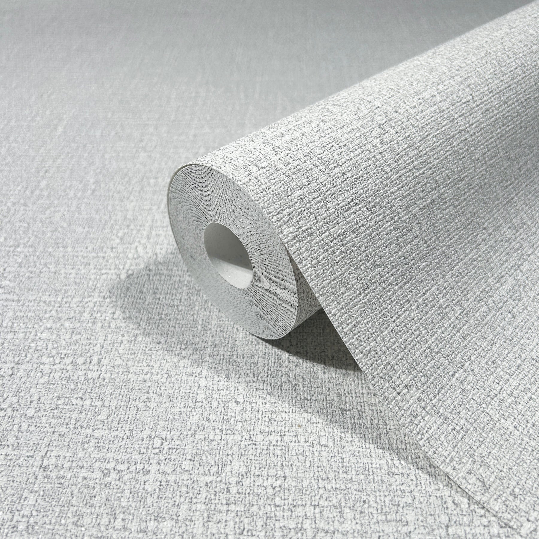 Gray textured wallpaper roll with woven fabric-like pattern, partially unrolled to reveal the cardboard core.