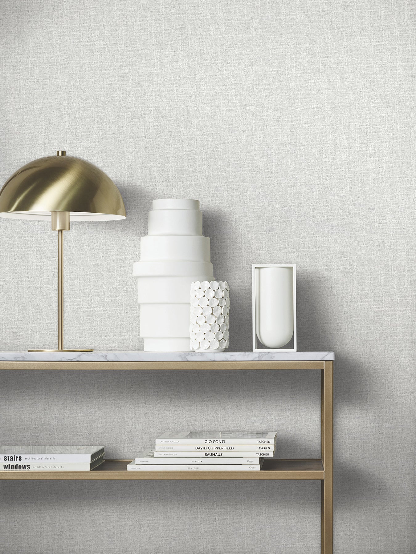 Brass dome lamp on marble shelf with white ceramic vases, smooth and pebbled textures, and a stack of design books.