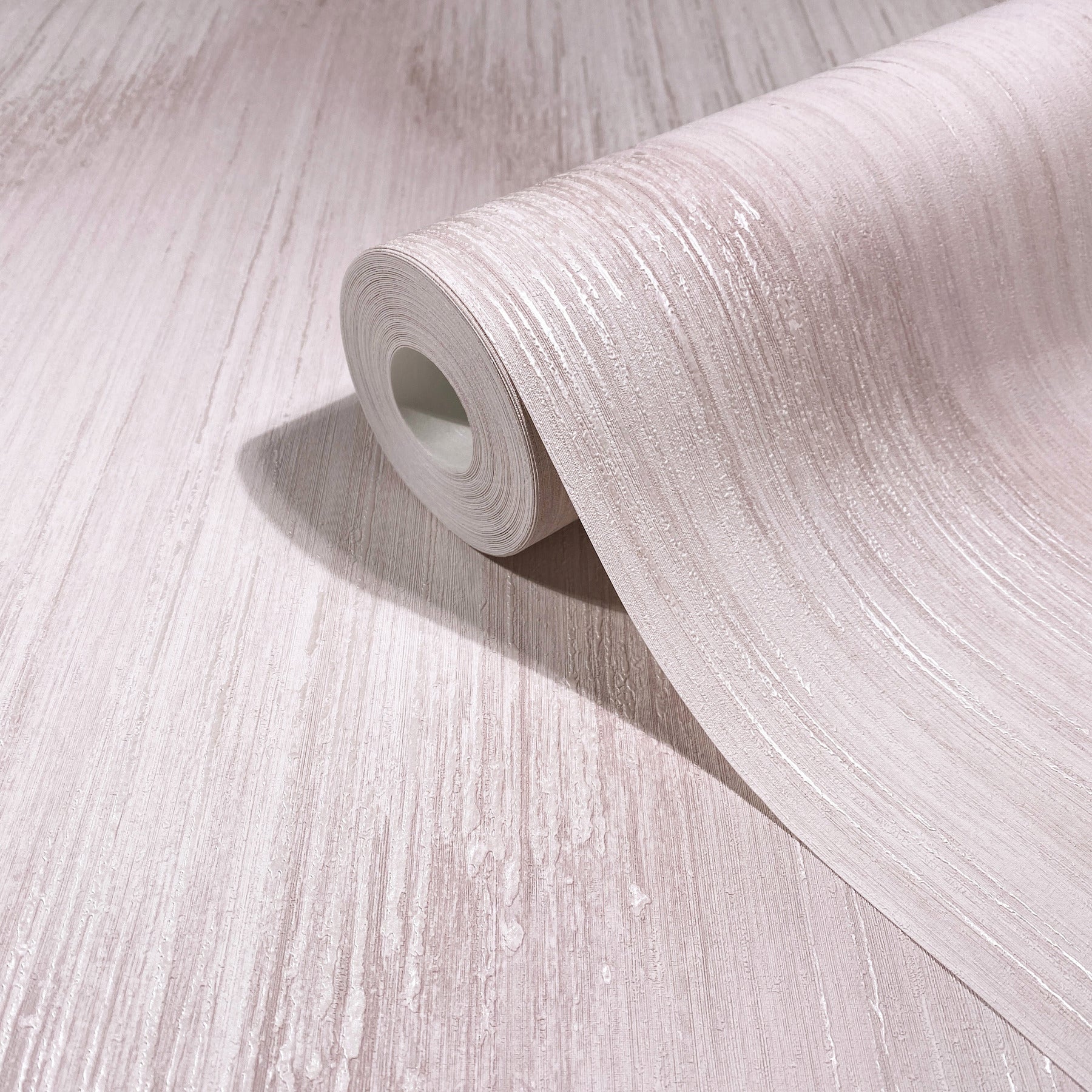 Roll of light beige wallpaper with subtle wood-grain texture, partially unrolled on pale wooden surface.
