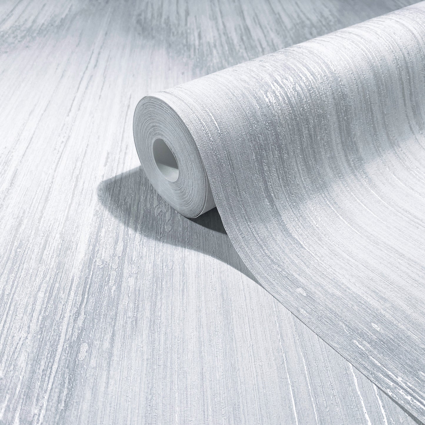 Silver metallic wallpaper roll with brushed texture, partially unrolled on a light gray surface.