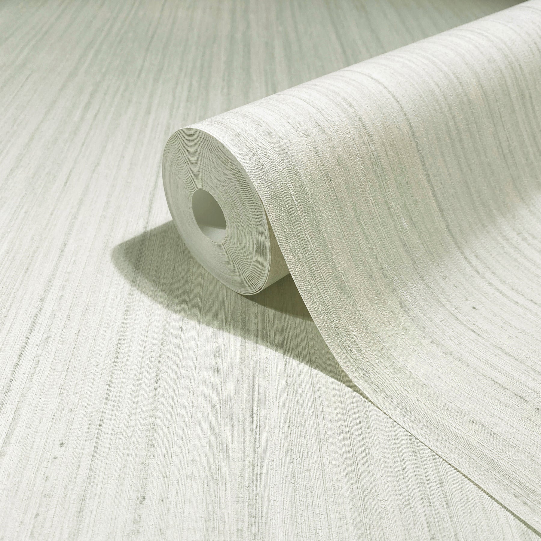 Light gray textured wallpaper roll unfurling on pale surface with subtle linear pattern.