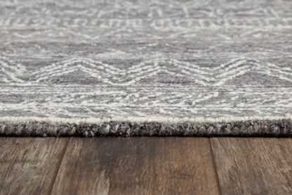 Gray patterned rug with fringe edge on wooden floor.