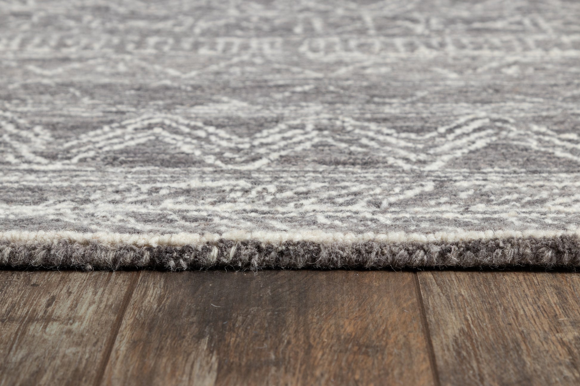 Gray and white patterned area rug with a fringe edge on dark wood floor, soft woven texture.