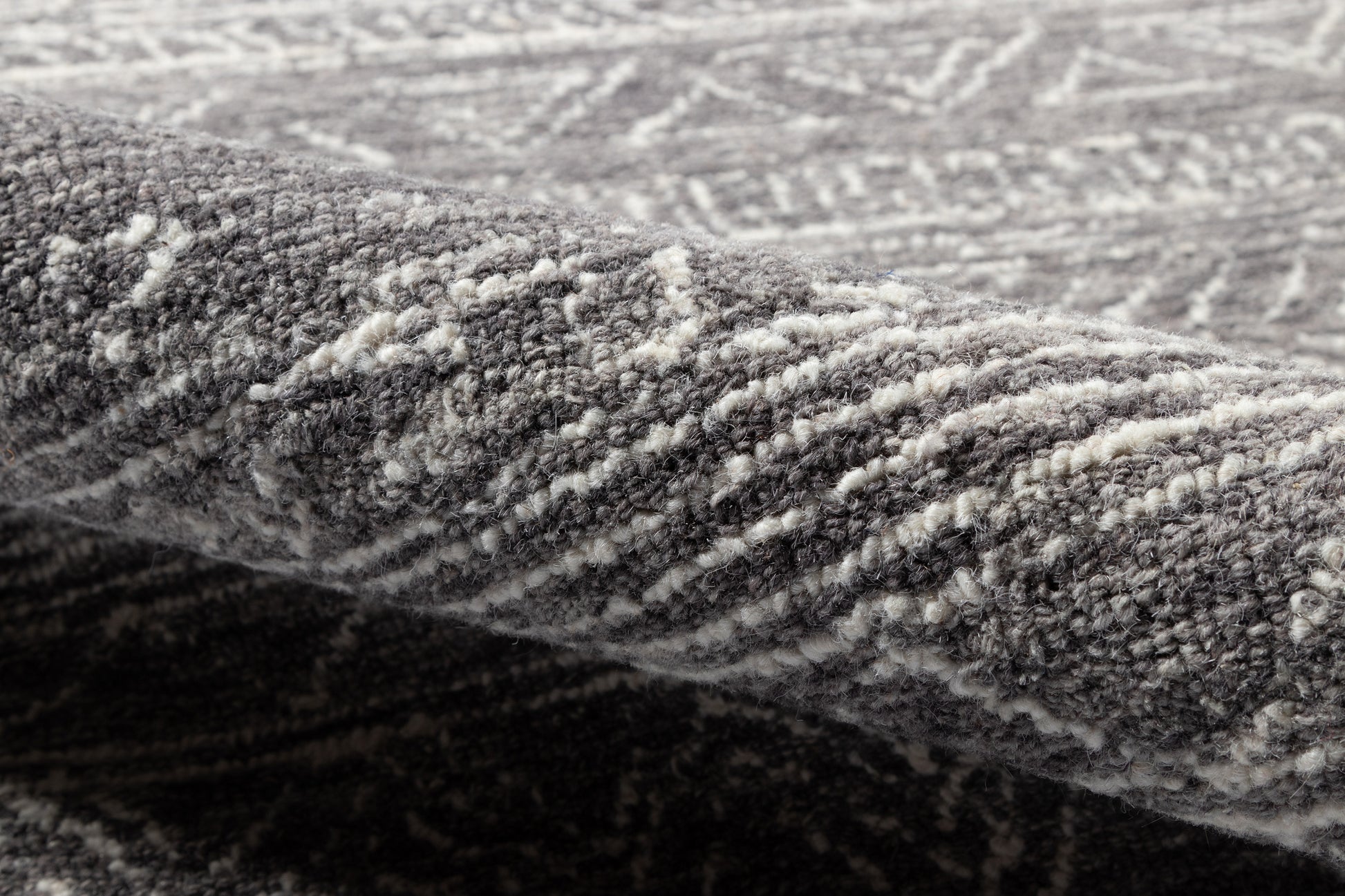 Grey patterned rug close-up with textured pile and folded edge; modern home decor.