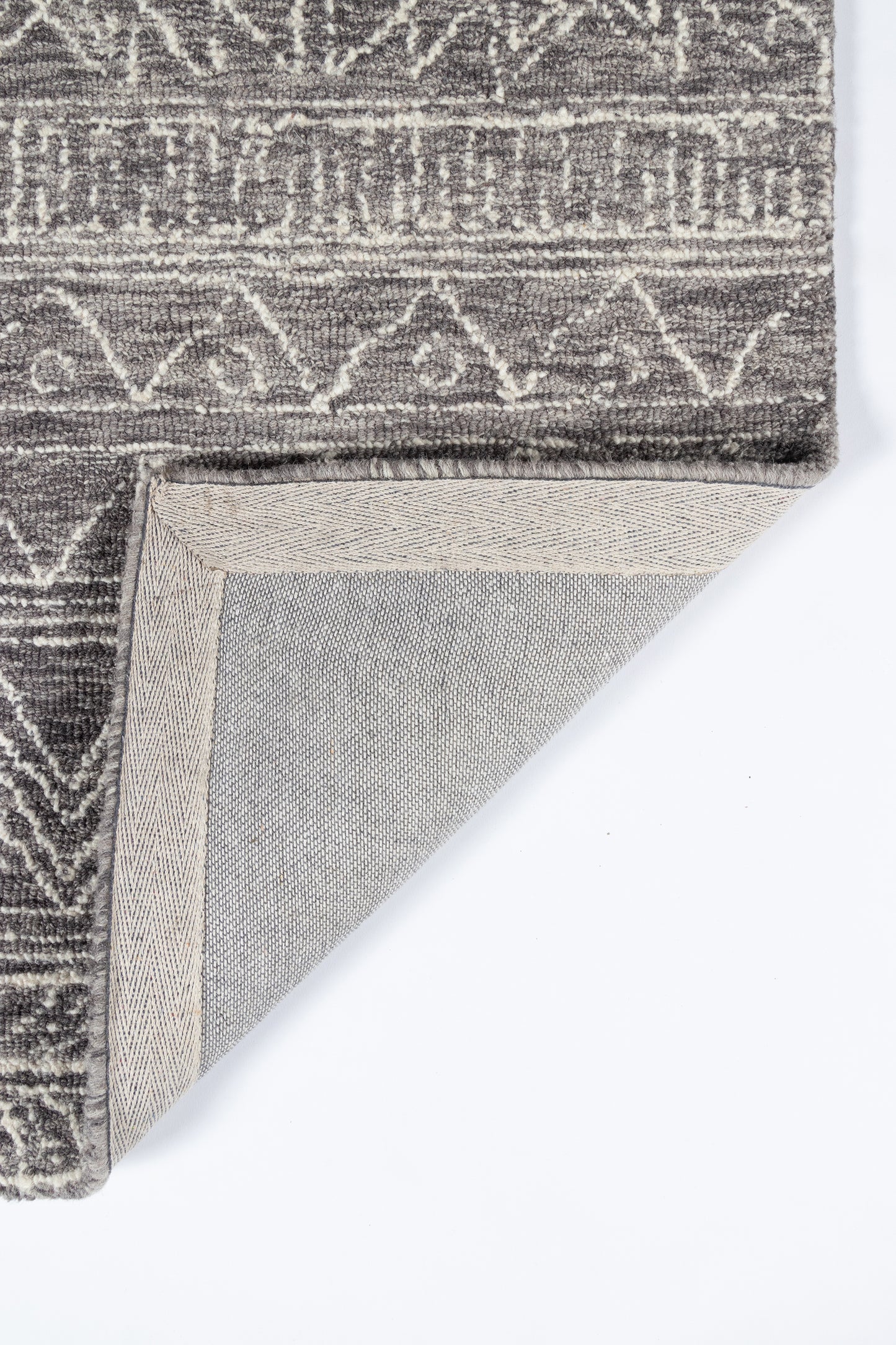Grey geometric patterned rug with woven texture; folded corner reveals beige underside, modern tribal style.