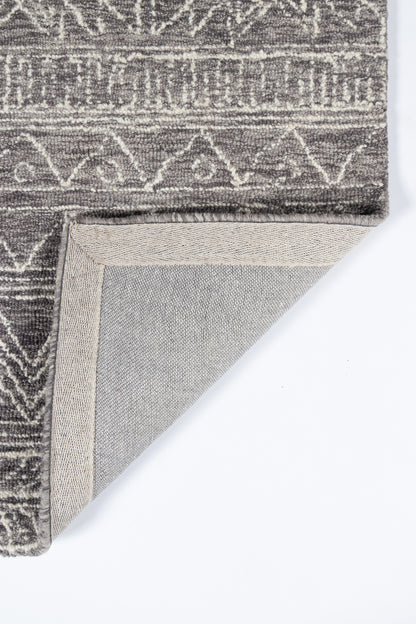 Grey geometric patterned rug with woven texture; folded corner reveals beige underside, modern tribal style.