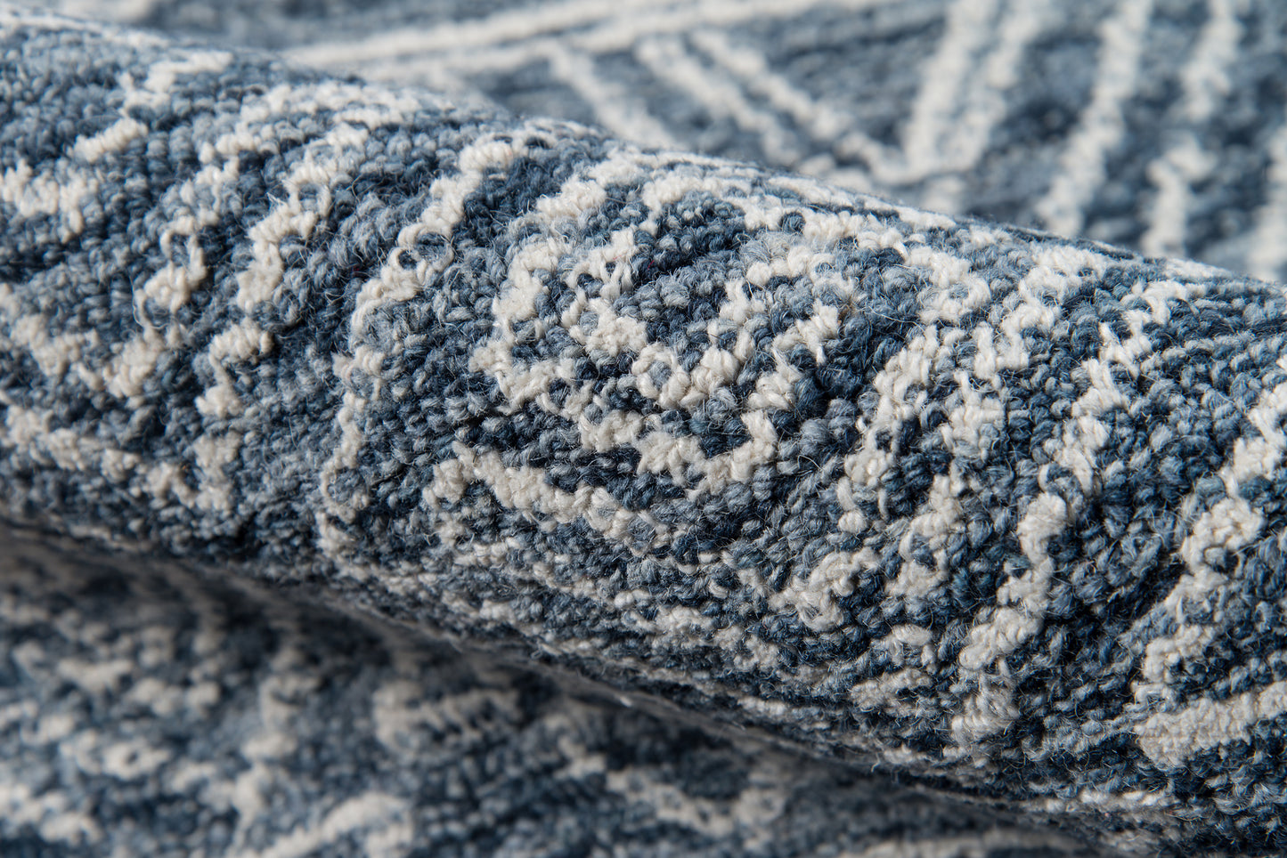 Blue-gray woven rug with white geometric diamond pattern; textured loop pile, close-up view.