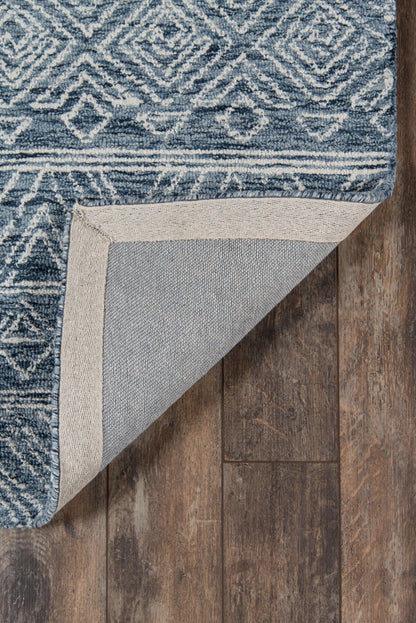 Blue and white geometric woven rug with a beige border; folded corner shows gray backing on dark wood floor.