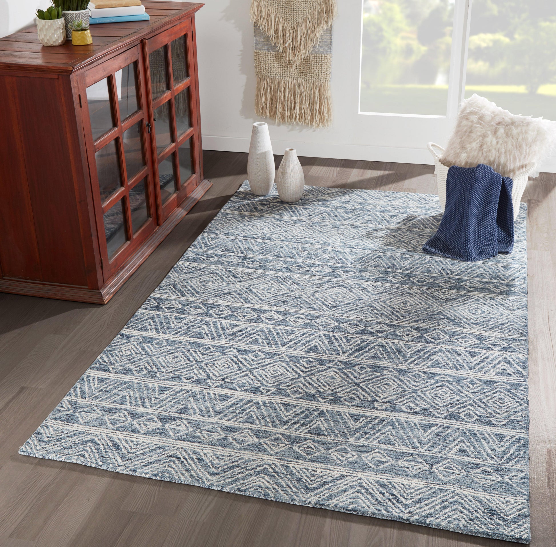 Blue and white geometric patterned runner rug on a dark hardwood floor, in a living room with a cabinet, vases, a chair, and a throw.
