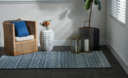 8' x 10' blue patterned rug with wicker chair, blue cushion, white vase of flowers, lanterns and a tall plant nearby.