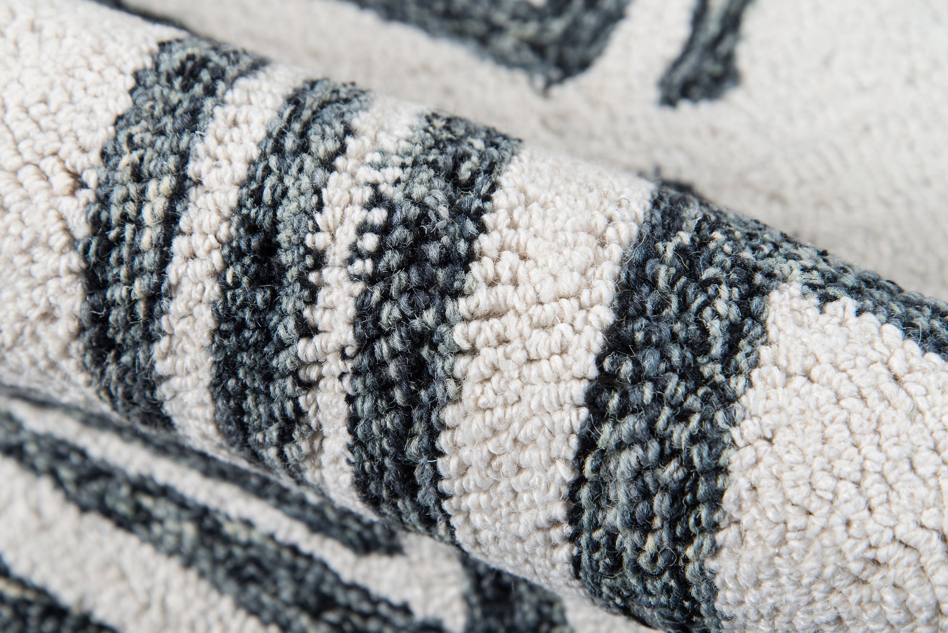 Close-up of a chunky woven rug with black, gray and cream stripes; textured boucle pile, rolled edge.