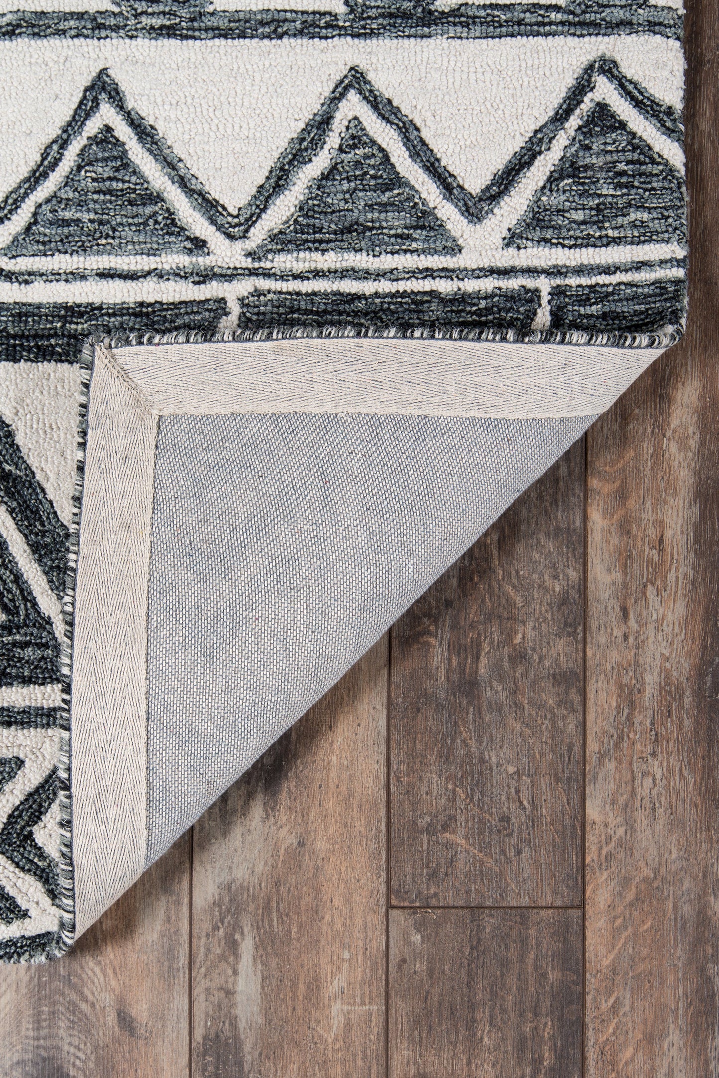Navy blue geometric triangle rug on wood floor; folded corner reveals beige backing, boho rustic style.