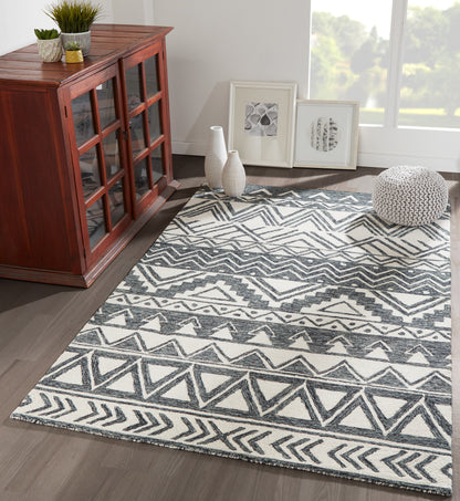 Gray and white geometric area rug with chevrons and triangles on a dark wood floor beside a red-toned cabinet.