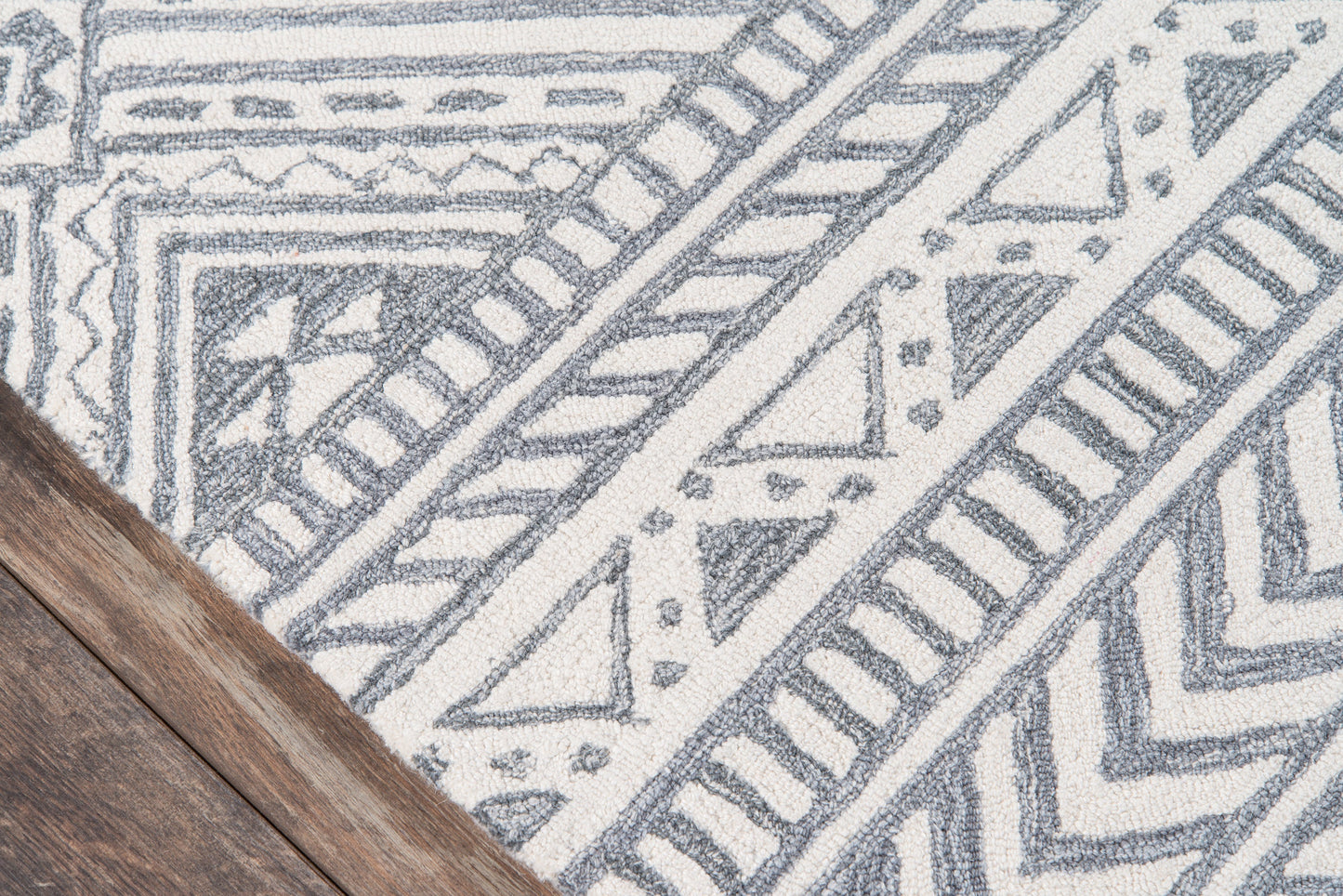 Gray and white geometric tribal-pattern rug with angular motifs; wooden floor corner visible.