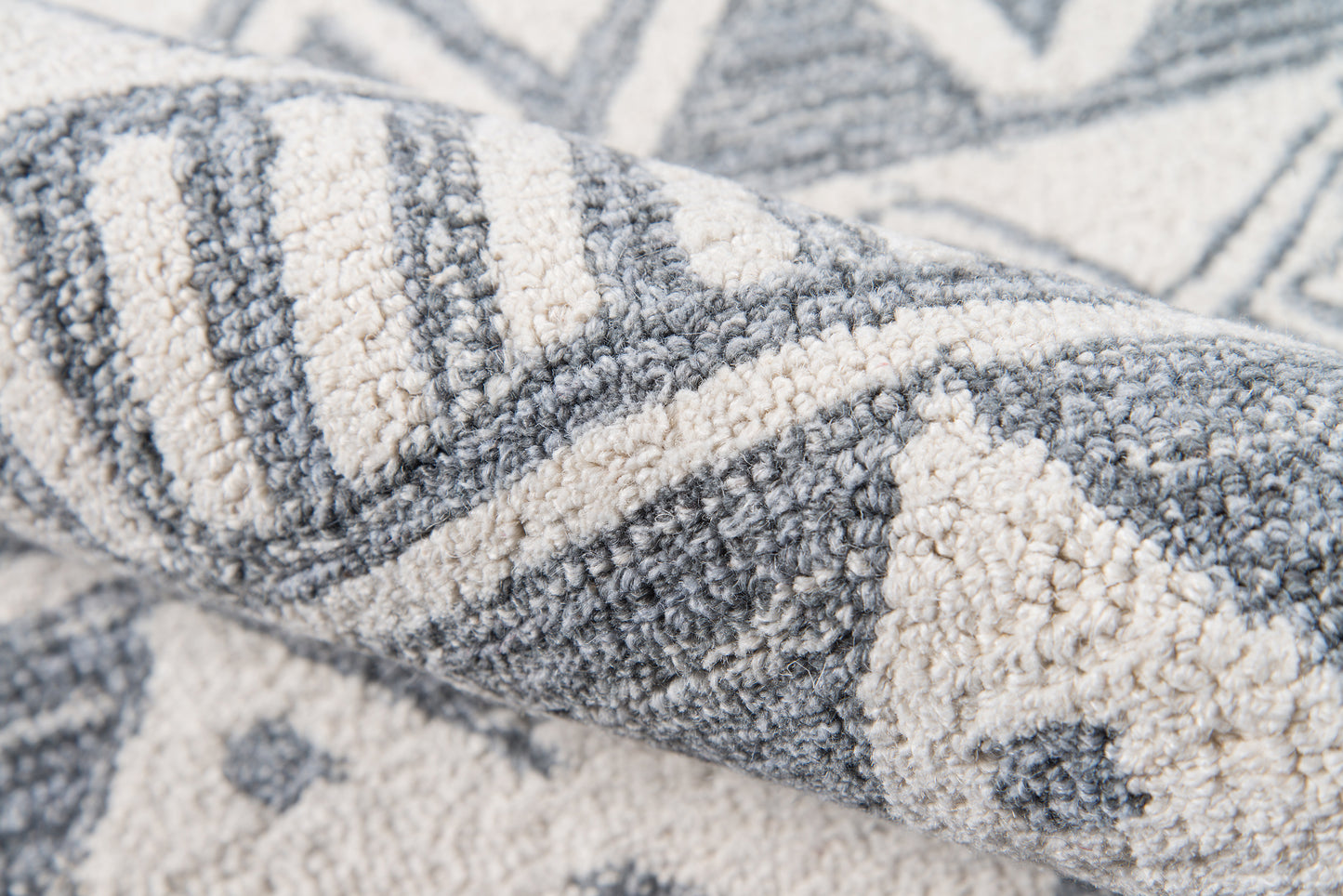 Close-up of a blue-gray and ivory geometric woven rug with striped and triangular patterns; soft textured fabric.