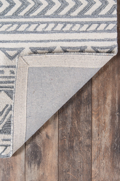 Gray geometric rug with chevron and border patterns, folded to reveal its light underside on a wooden floor.