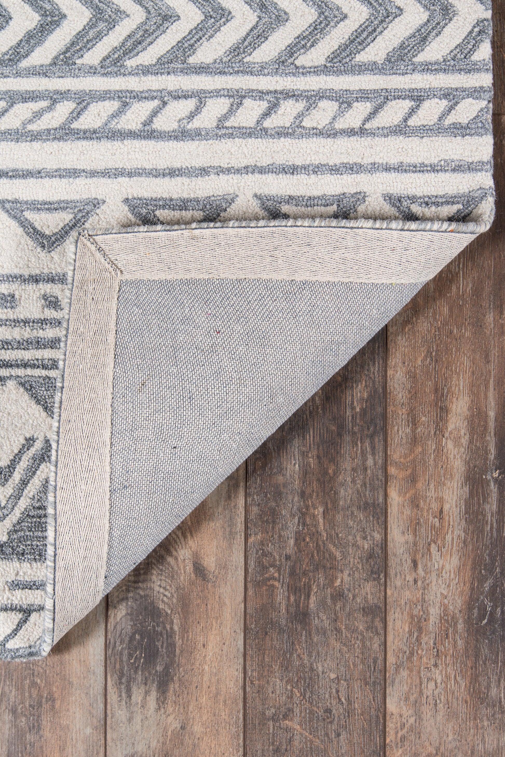Gray geometric rug with chevron and stripe patterns, folded corner shows light backing on dark wood floor