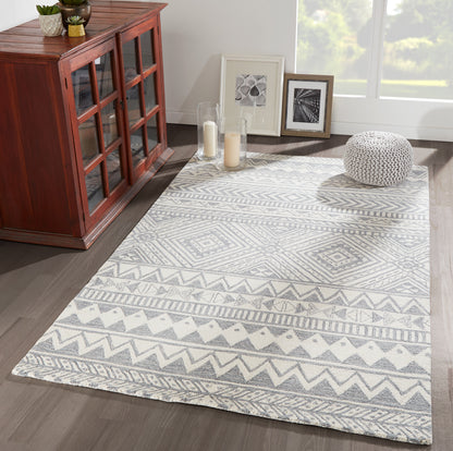 Gray and white geometric area rug with chevrons and diamonds in a living room with a wooden cabinet and framed art.