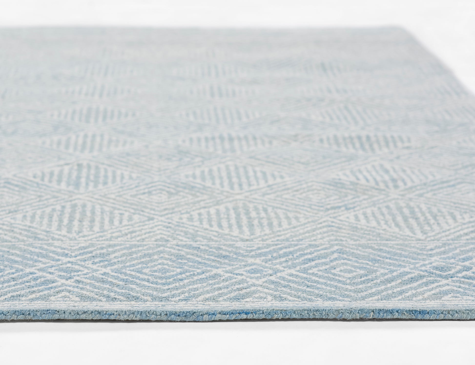 Blue and white flatweave rug with geometric diamond pattern, close-up edge view.